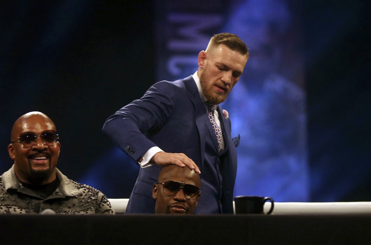 Irish boxer Connor McGregor, background, touches US boxer Floyd Mayweather Jr on the head, during a press conference to promote their upcoming fight, at the SSE Arena